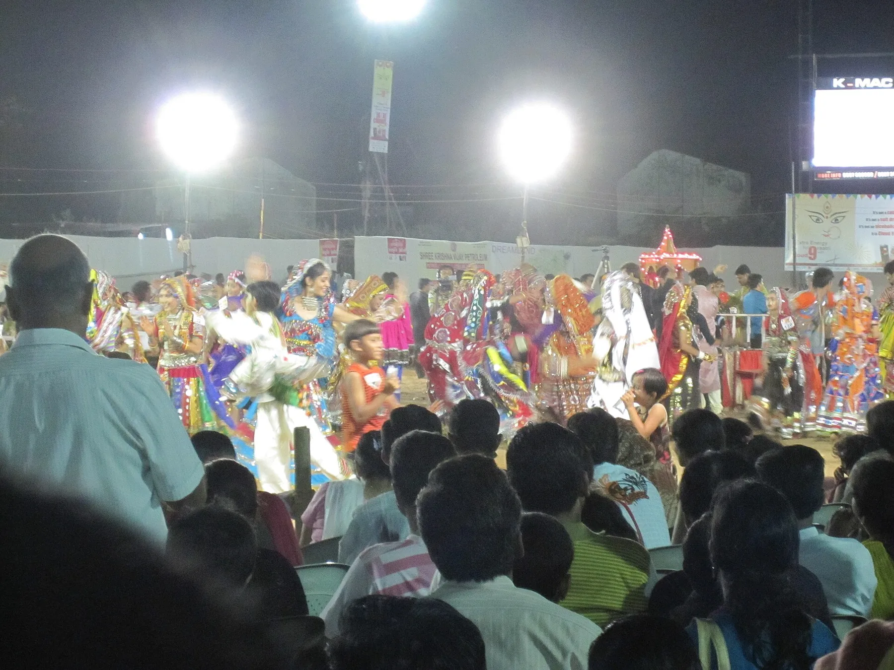 A large Garba crowd dancing under floodlights
